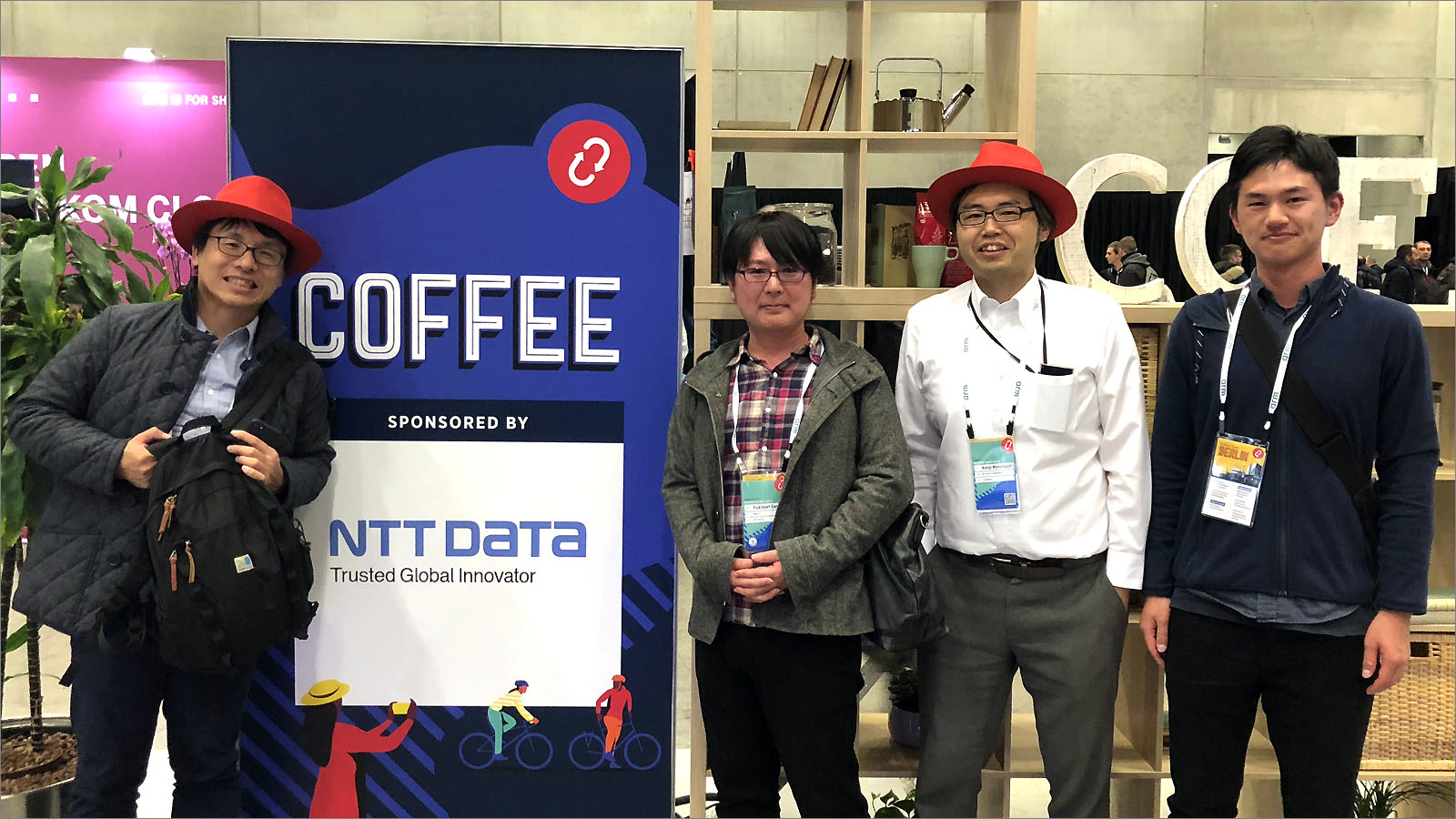 NTTデータのコーヒースポンサーパネル前の一枚。赤い帽子は、Red Hatが参加者へ無料で配布していたもの(左から田代充良、相良幸範、本橋賢二、村中清史)